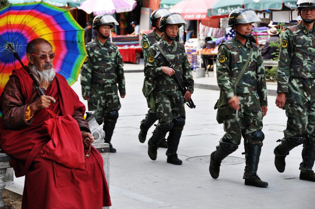 Monk in Lhasa with Chinese military marching past. 
