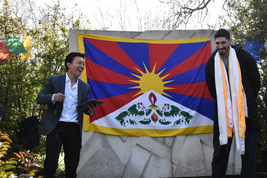 Enes Kanter Freedom and a Tibetan community representative laugh together as they stand in front of the Tibetan flag.