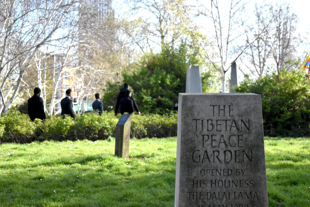 In the foreground: the sign to the Tibetan Peace Garden, carved in stone. In the background Enes Kanter Freedom and his team can be seen entering the garden.