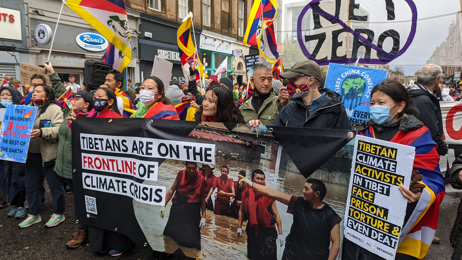 Tibetan activists march at COP26 in Glasgow, carrying banners and Tibetan flags.