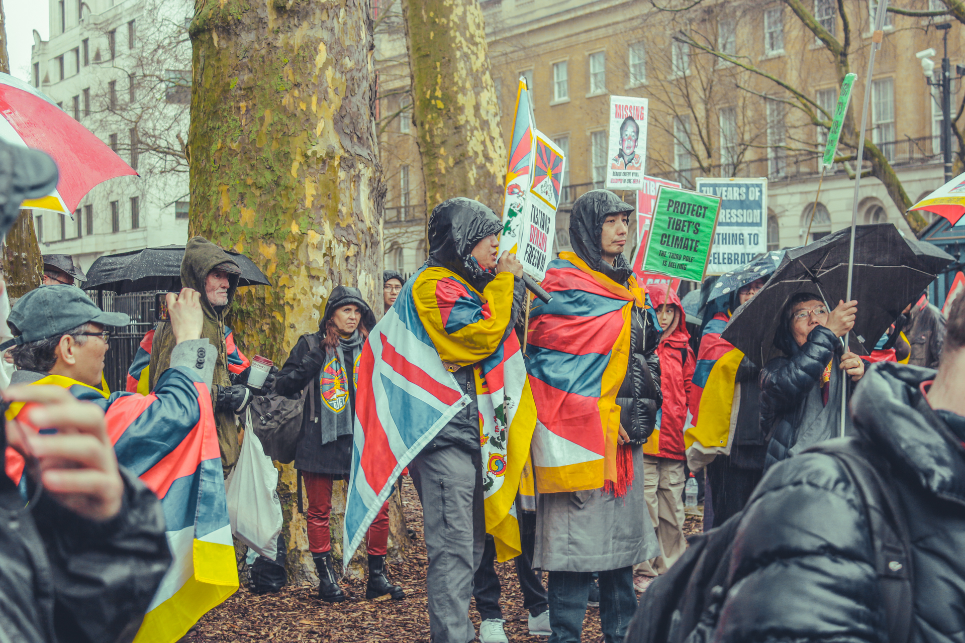 Tibetan activists, wearing both UK and Tibetan flags over their shoulders, give speeches outside 10 Downing Street.